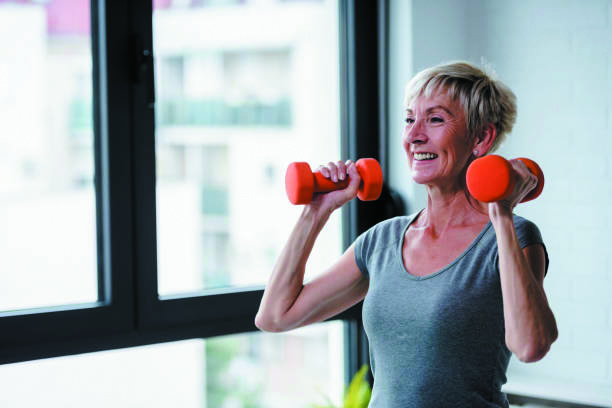 Active good looking elderly woman smiling and holding dumbbells while working out indoors